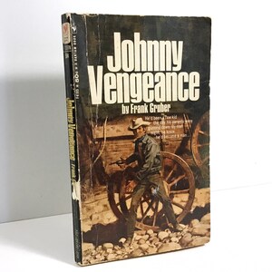 May include: A vintage paperback book cover with a brown and white illustration of a man in a cowboy hat holding a gun. The book title is "Johnny Vengeance" by Frank Gruber.