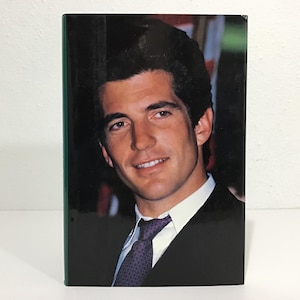 May include: A book with a portrait of a man in a suit and tie. The man has dark hair and is smiling. The book has a green spine and is set against a white background.