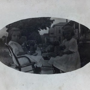 Affascinante RPPC di 2 ragazze carine con orsacchiotti e bambole seduti sul portico esterno, case di quartiere c.1910 - Antica cartolina fotografica reale