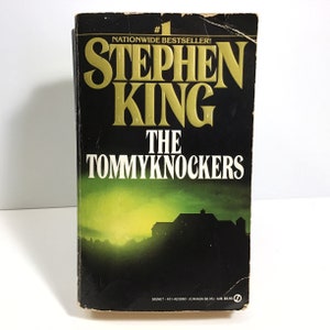 May include: A paperback book cover with a green and black background. The title is "The Tommyknockers" by Stephen King. The book is a #1 nationwide bestseller.