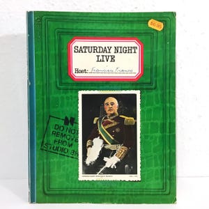May include: A vintage book with a green cover featuring the text "SATURDAY NIGHT LIVE" and "Host: Francisco Franco." A postage stamp-like image of a man in uniform is below the text. A sticker indicates the price is $6.95.