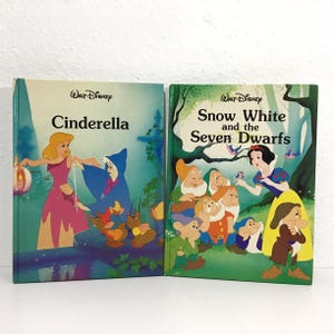 May include: Two vintage Walt Disney storybooks: "Cinderella" and "Snow White and the Seven Dwarfs." The "Cinderella" book features a pink-clad character with blonde hair. The "Snow White" book shows Snow White with the seven dwarfs. Both books have colorful illustrations.