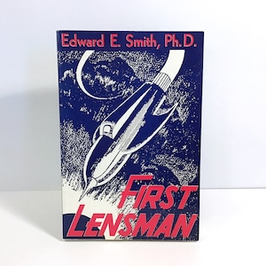 May include: A blue and white book cover with a red title that reads "First Lensman". The cover features a black and white illustration of a rocket ship flying through space.