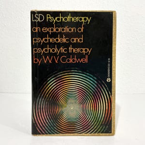May include: A paperback book titled LSD Psychotherapy: an exploration of psychedelic and psycholytic therapy by W.V. Caldwell. The black cover features a large, colorful, circular optical illusion pattern and the Evergreen E-510 logo.