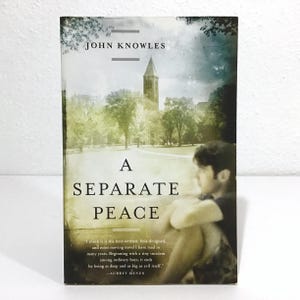 May include: A paperback book titled "A Separate Peace" by John Knowles. The cover features a scenic view of a building and trees, with a silhouette of a person. The book has a quote by Aubrey Menen.