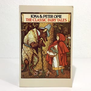 May include: A vintage book cover for "The Classic Fairy Tales" by Iona & Peter Opie. The cover features an illustration of Little Red Riding Hood and the wolf in a forest setting. The title is in a banner at the top.