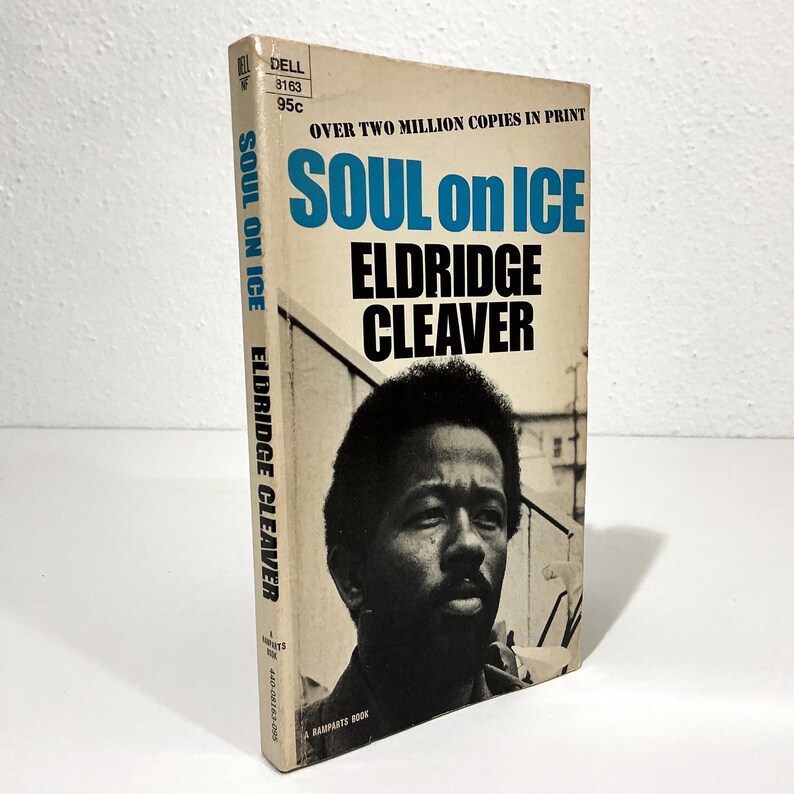 Puede incluir: Un libro de bolsillo titulado Soul on Ice de Eldridge Cleaver, publicado por Dell. La portada presenta un retrato en blanco y negro de un hombre, con el t&iacute;tulo en texto azul negrita y el nombre del autor en negro. Indica m&aacute;s de dos millones de copias.