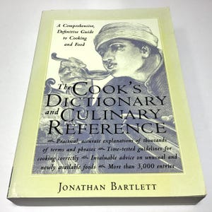 May include: A hardcover book titled "The Cook's Dictionary and Culinary Reference" by Jonathan Bartlett. The cover features an illustration of a person holding a spoon, with text describing it as a comprehensive guide to cooking and food.