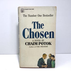 May include: A paperback book cover with a white background and blue text. The title is "The Chosen" by Chaim Potok, author of "The Promise". The cover features a black and white illustration of three men in traditional Jewish clothing.