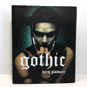 May include: A book cover with a dark, gothic theme. The cover features a person with dark makeup and a black outfit. The word "gothic" is in a stylized white font, with "dark glamour" below it.