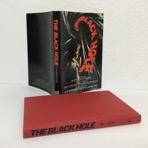 Op de afbeelding: Een hardcover boek getiteld "The Black Hole" met een rode kaft en rug. De kaft van het boek heeft een zwarte achtergrond met de titel in oranje en wit, en de naam van de auteur. Het boek is een roman gebaseerd op de film van Walt Disney Productions.