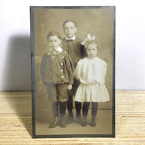 Antike echte Fotopostkarte – 3 edwardianische Kinder, Brüder und Schwester – Geisterkinder, verschwindendes, heimgesuchtes Foto, RPPC aus dem frühen 20. Jahrhundert