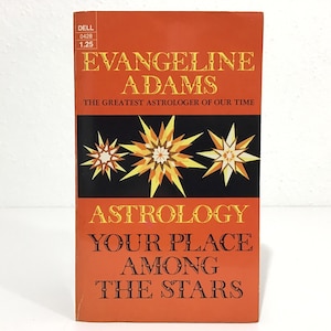 May include: A vintage paperback book titled "Astrology Your Place Among The Stars" by Evangeline Adams. The cover is orange with black and yellow starburst designs. The book is a Dell publication, with the price of $1.25.