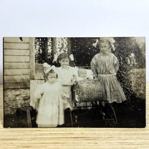 Antieke echte foto ansichtkaart - 3 Edwardiaanse meisjes & baby in kinderwagen - schattige kleine meisjes met GROTE witte strikken in haar, begin 1900 RPPC