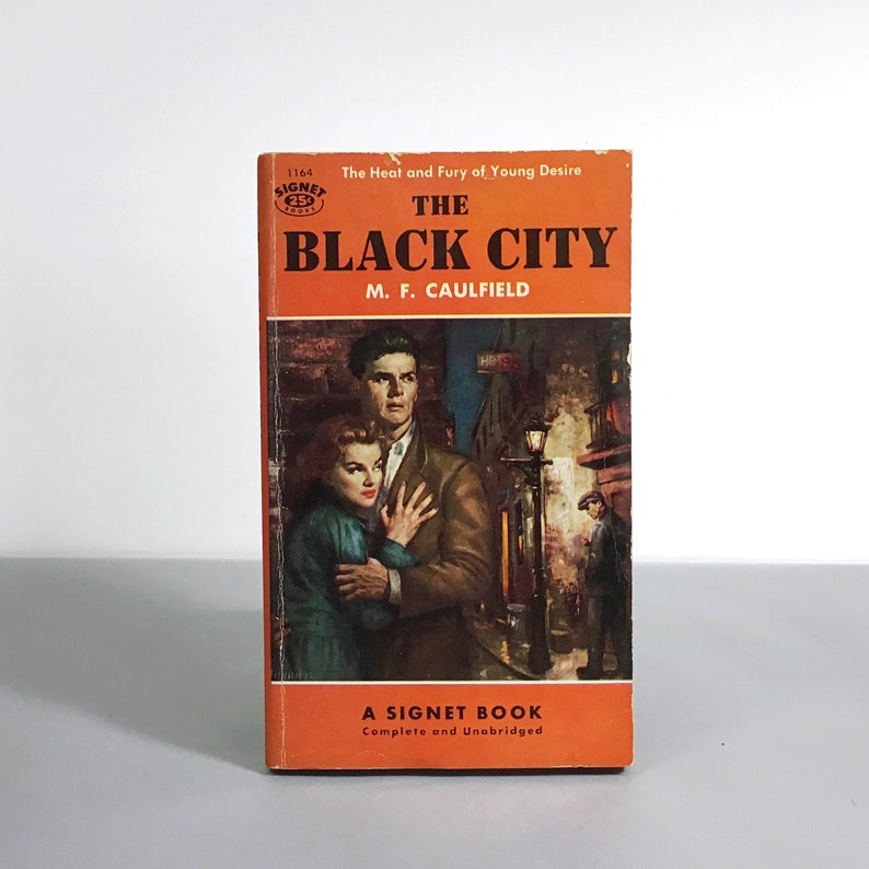 K&ouml;nnte beinhalten: Ein Vintage-Taschenbuch mit dem Titel "The Black City" von M. F. Caulfield. Das Cover zeigt ein Paar, das sich in einer schwach beleuchteten Stadtstra&szlig;e umarmt. Das Buch ist eine Signet-Publikation.