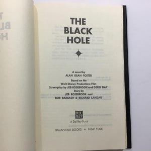 Op de afbeelding: Open boek met de titel "THE BLACK HOLE" in dikke zwarte letters. De naam van de auteur, Alan Dean Foster, staat eronder. Gebaseerd op de Walt Disney Productions Film. Uitgegeven door Ballantine Books, New York.