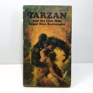 May include: A vintage paperback book cover featuring a dramatic illustration of Tarzan fighting a gorilla in a jungle setting. The title reads "Tarzan and the Lion Man" by Edgar Rice Burroughs. The book is part of the Tarzan series, number 17.