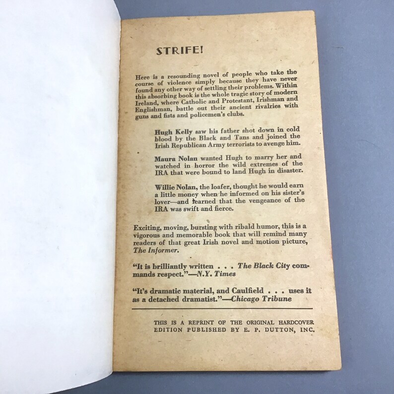 K&ouml;nnte beinhalten: Ein Vintage-Taschenbuchcover mit wei&szlig;em Hintergrund und schwarzem Text. Der Titel des Buches lautet "STRIFE!" und der Text beschreibt das Buch als einen "ersch&uuml;tternden Roman" &uuml;ber die Irische Republikanische Armee. Das Buch ist ein Nachdruck der urspr&uuml;nglichen Hardcover-Ausgabe, die von E.P. Dutton, Inc. ver&ouml;ffentlicht wurde.