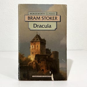 May include: A paperback book titled Dracula by Bram Stoker from the Wordsworth Classics series. The cover features a painting of a stone castle under a cloudy sky. The text reads Wordsworth Classics, Bram Stoker, Dracula, and Complete and Unabridged.