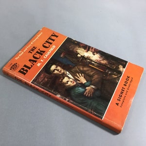 K&ouml;nnte beinhalten: Ein Vintage-Taschenbuch mit dem Titel "The Black City" von M.F. Caulfield. Das Cover zeigt eine dramatische Illustration eines Mannes und einer Frau in einem schwach beleuchteten Raum. Das Buch ist ein Signet Book, vollst&auml;ndig und ungek&uuml;rzt.