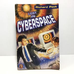 May include: A paperback book titled "Lost in Cyberspace" by Richard Peck. The cover features two boys in front of computer monitors with a bright orange and yellow background. The book is published by Penguin.