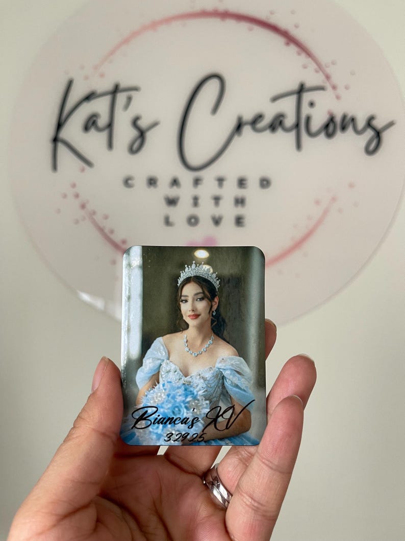 Puede incluir: Un im&aacute;n fotogr&aacute;fico rectangular con una mujer con un vestido azul claro, tiara y collar. El texto "Bianca's XV 3.29.25" est&aacute; escrito en el im&aacute;n. El fondo incluye un logotipo que dice "Kat's Creations".