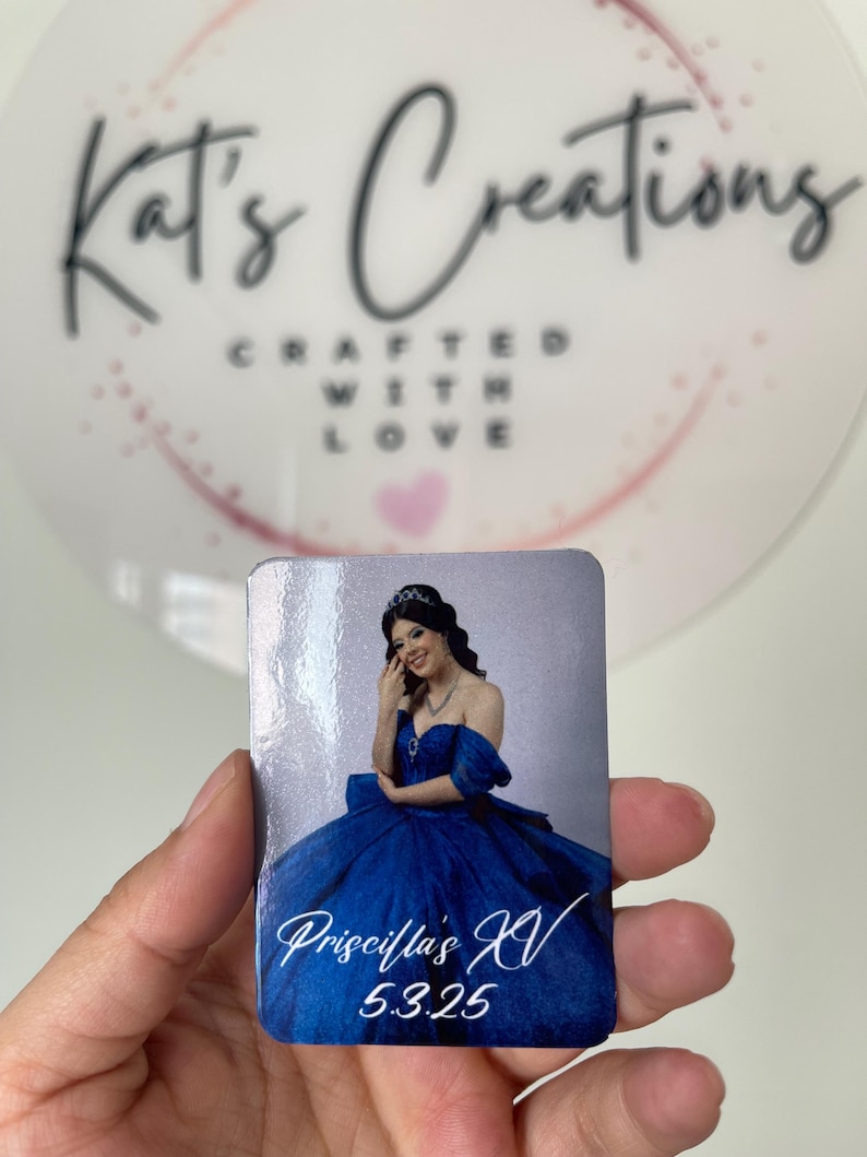 Puede incluir: Un im&aacute;n rectangular con una joven con un vestido de baile azul real. El im&aacute;n tiene el texto "Priscilla's XV 5.3.25" en escritura blanca. El fondo es una imagen borrosa de un c&iacute;rculo blanco con el texto "Kat's Creations Crafted With Love."