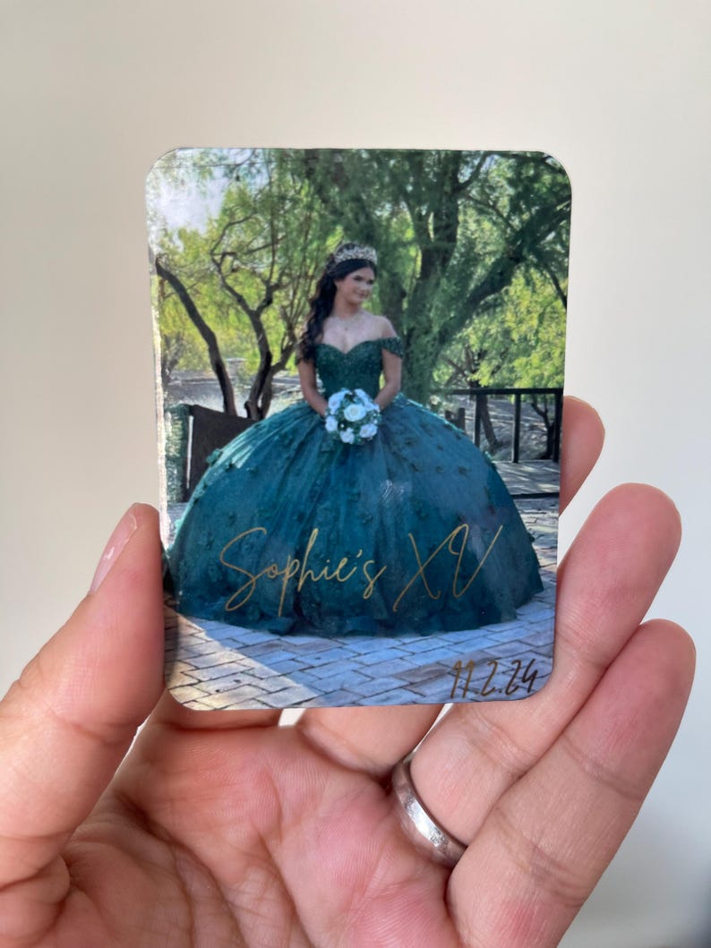 Puede incluir: Un im&aacute;n rectangular con una joven en un vestido de quincea&ntilde;era verde azulado, sosteniendo un ramo. El im&aacute;n tiene el texto "Sophie's XV" en escritura dorada, con la fecha "11.2.24" debajo. El fondo muestra un puente y &aacute;rboles.