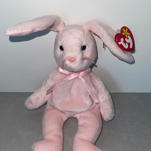 May include: Pink plush bunny rabbit with a pink ribbon around its neck. The bunny has a Ty tag attached to its ear that says "Beanie Babies".