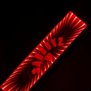 May include: A red neon sign with the words "SADBOYZ" and a broken heart symbol. The sign is made of LED lights and has a mirrored effect.
