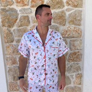 May include: White pajamas with a short-sleeved shirt and shorts. The shirt and shorts have a repeating pattern of cartoon characters wearing Santa hats and holding presents. The pattern is on a white background with red trim.