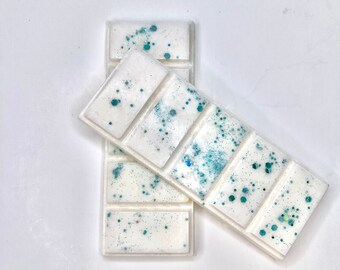 May include: Two white wax melts with teal glitter. The wax melts are in a grid pattern and are stacked on top of each other.