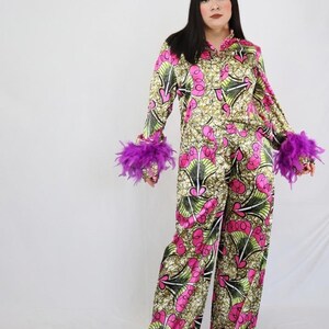Puede incluir: Un conjunto de camisa de manga larga con botones y pantalones anchos a juego, con un estampado geométrico en rosa vibrante, verde lima y beige. Los puños de las mangas largas están adornados con detalles de plumas moradas.