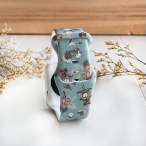 Könnte beinhalten: Ein hellblaues Armband mit einem fantasievollen Weihnachtsmotiv mit Feen, Uhren und Geschenken. Das Armband ist aus Silikon und hat eine weiße Schließe.
