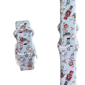May include: A blue and white patterned watch band with a Nutcracker and ballerina design. The band is made of silicone and has a buckle closure.