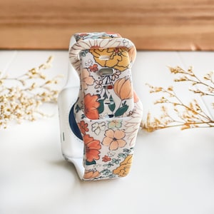 Może przedstawiać: Biały silikonowy pasek do zegarka z nadrukiem kwiatowym w kolorze pomarańczowym, żółtym i zielonym. Pasek jest przeznaczony do smartwatcha.