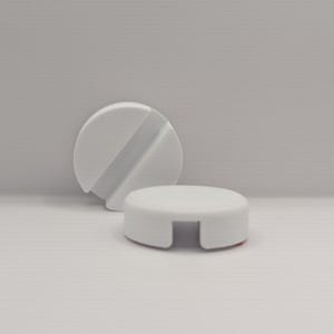 Op de afbeelding: Twee witte, ronde telefoonstandaards. Eén standaard staat rechtop met een diagonale groef, de andere is een platte schijf met twee uitgesneden secties. De standaards zijn gemaakt van een glad, stevig materiaal.