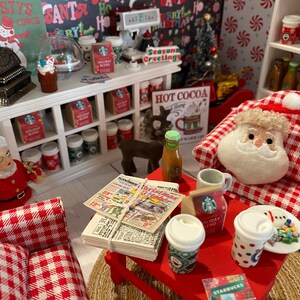 Pode incluir: Uma loja de Natal em miniatura com uma poltrona xadrez vermelha e branca, uma mesa vermelha com uma pilha de jornais e uma boneca do Papai Noel. A loja tem um balc&atilde;o branco com prateleiras cheias de itens de Natal em miniatura, incluindo x&iacute;caras de caf&eacute;, bengalas de doces e um caixa registradora.