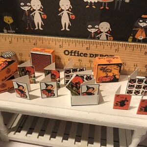 Puede incluir: Un conjunto de tarjetas de Halloween en miniatura con gatos negros, brujas y calabazas. Las tarjetas est&aacute;n dispuestas sobre una mesa blanca con una regla de madera y una peque&ntilde;a caja de tarjetas de Halloween.