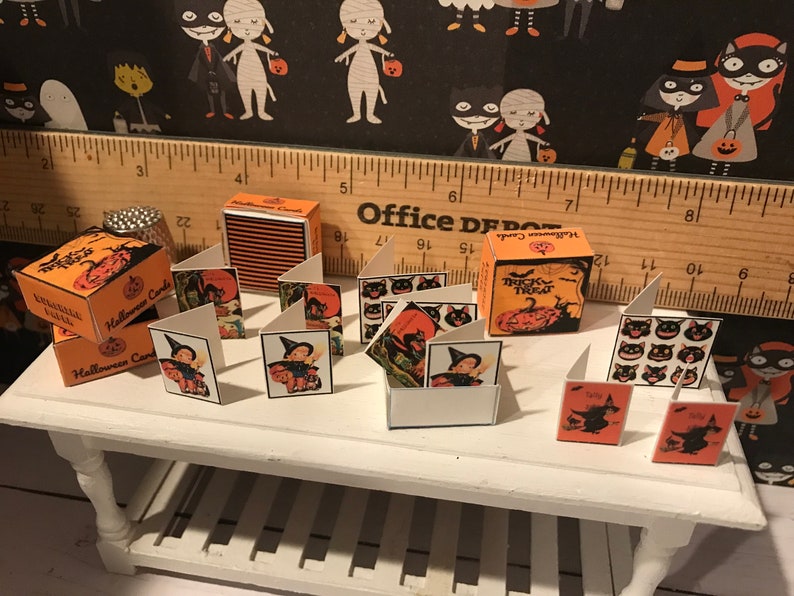 Puede incluir: Un conjunto de tarjetas de Halloween en miniatura con gatos negros, brujas y calabazas. Las tarjetas est&aacute;n dispuestas sobre una mesa blanca con una regla de madera y una peque&ntilde;a caja de tarjetas de Halloween.