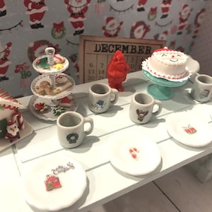 May include: A miniature Christmas scene with a gingerbread house, a tiered cake stand with Christmas cookies, and a white cake with a red Santa hat. There are also miniature mugs and plates with Christmas designs.