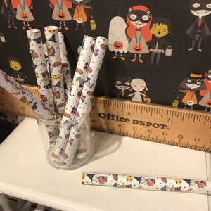 Puede incluir: Un juego de pajitas de papel blancas con un estampado de Halloween con personajes negros y naranjas. Las pajitas est&aacute;n en un vaso transparente sobre una mesa blanca con una regla de madera que dice "Office Depot".