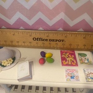 May include: A miniature white hat with a white ribbon and yellow flowers, a small white book with the words "Holy Bible" on the cover, four colorful Easter eggs, and four miniature books with Easter themes. The books have titles like "Springtime Fun" and "Happy Easter Mouse".