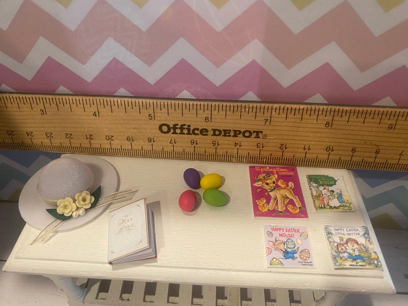 May include: A miniature white hat with a white ribbon and yellow flowers, a small white book with the words "Holy Bible" on the cover, four colorful Easter eggs, and four miniature books with Easter themes. The books have titles like "Springtime Fun" and "Happy Easter Mouse".