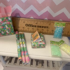 May include: A set of Easter-themed wrapping paper, gift boxes, and Easter grass. The wrapping paper features a green and pink pattern with bunnies and eggs. The gift boxes are decorated with a floral pattern. The Easter grass is blue and green.