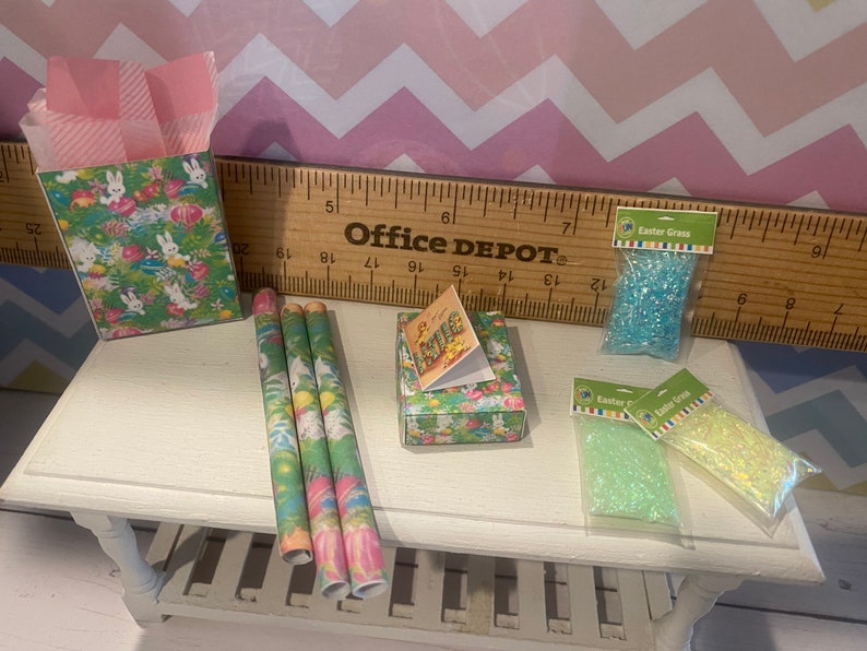 May include: A set of Easter-themed wrapping paper, gift boxes, and Easter grass. The wrapping paper features a green and pink pattern with bunnies and eggs. The gift boxes are decorated with a floral pattern. The Easter grass is blue and green.