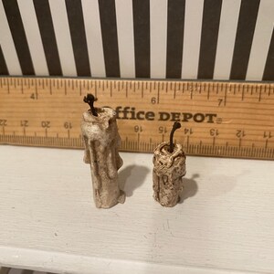 May include: Two small, off-white, textured candles with dark wicks. One candle is taller than the other. A wooden ruler with black markings and the text "office DEPOT" is in the background.