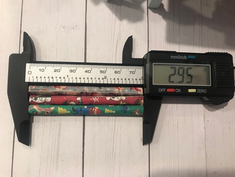Puede incluir: Un calibre digital negro que mide tres pajitas de papel de colores con tem&aacute;tica navide&ntilde;a. El calibre muestra 2,95 pulgadas.