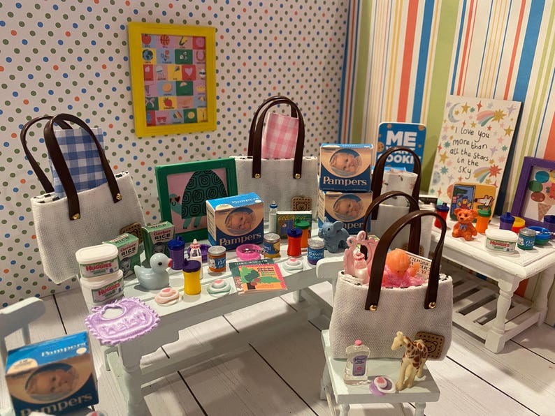 May include: A miniature scene featuring baby products, including Pampers diapers, baby bottles, and a bib. Several tote bags with brown handles are present, along with a framed picture and a sign that reads "I love you more than all the stars in the sky."