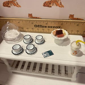 Pode incluir: Mesa branca em miniatura com um conjunto de x&iacute;caras e pires, um prato de sobremesa com biscoitos e um cart&atilde;o-presente Starbucks. Uma c&uacute;pula transparente e uma bebida com canudo amarelo tamb&eacute;m est&atilde;o na mesa. O fundo apresenta uma r&eacute;gua e estampa de tigre.